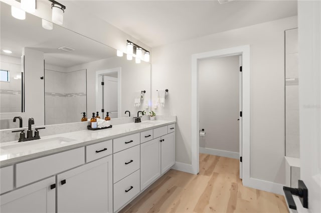 bathroom with wood-type flooring, tiled shower, and vanity