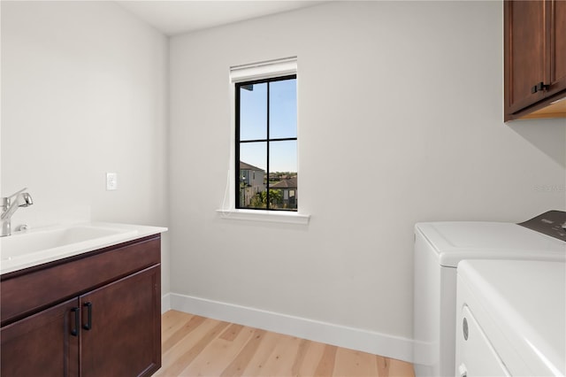 laundry room with light hardwood / wood-style floors, cabinets, separate washer and dryer, and sink