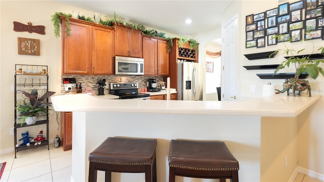 kitchen with light tile patterned flooring, appliances with stainless steel finishes, a kitchen breakfast bar, kitchen peninsula, and backsplash