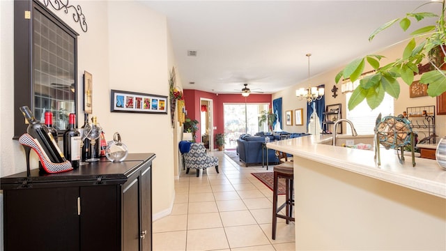 kitchen featuring light tile patterned floors, ceiling fan with notable chandelier, hanging light fixtures, and a kitchen bar