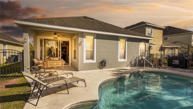 pool at dusk featuring ceiling fan, an outdoor living space, and a patio area