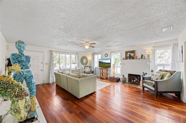 living room with dark hardwood / wood-style flooring, ceiling fan, plenty of natural light, and a textured ceiling