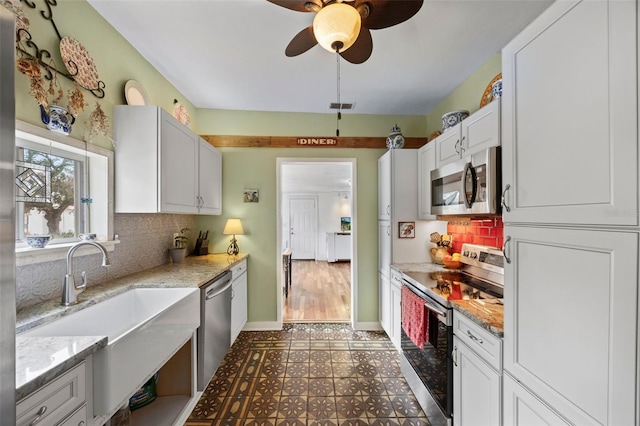 kitchen with sink, white cabinetry, light stone counters, stainless steel appliances, and backsplash