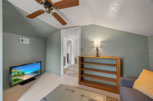 living area featuring ceiling fan, lofted ceiling, light hardwood / wood-style flooring, and a textured ceiling