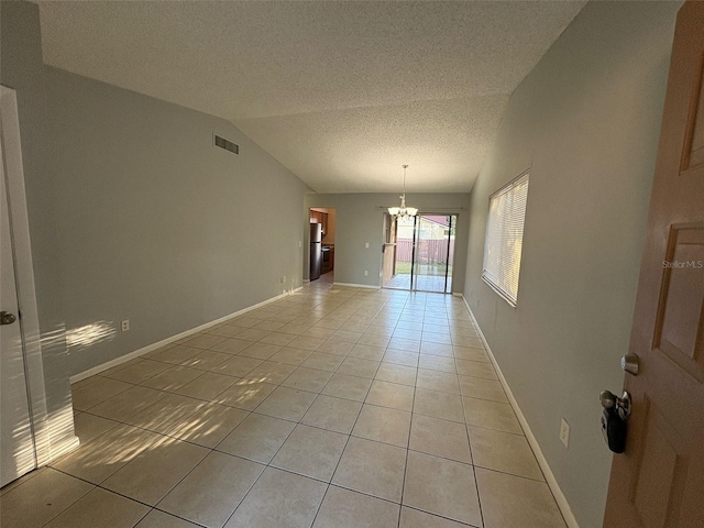 empty room featuring lofted ceiling, a notable chandelier, a textured ceiling, and light tile patterned flooring