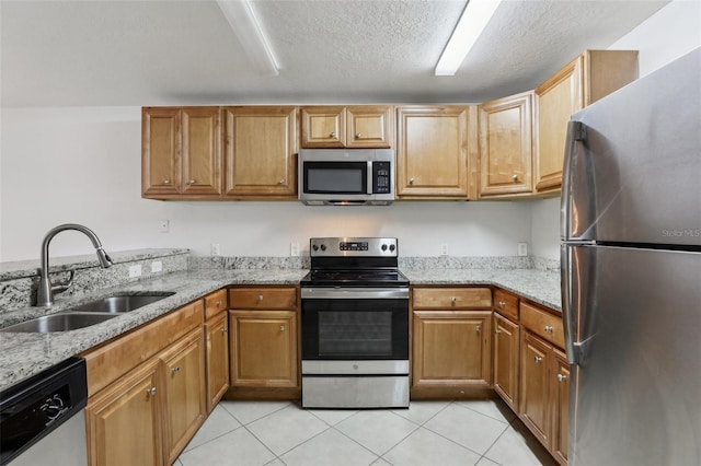 kitchen with sink, light tile patterned floors, light stone countertops, a textured ceiling, and stainless steel appliances