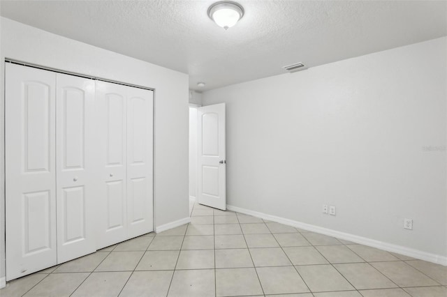 unfurnished bedroom featuring a textured ceiling, a closet, and light tile patterned floors