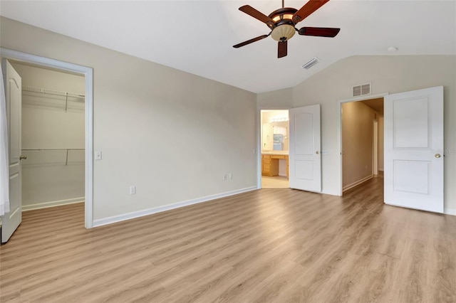 unfurnished bedroom featuring ceiling fan, a walk in closet, light hardwood / wood-style floors, a closet, and lofted ceiling