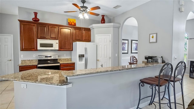 kitchen with kitchen peninsula, light tile patterned floors, ceiling fan, light stone counters, and white appliances