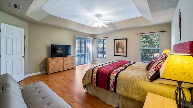 bedroom featuring light hardwood / wood-style flooring, ceiling fan, a textured ceiling, access to outside, and a raised ceiling