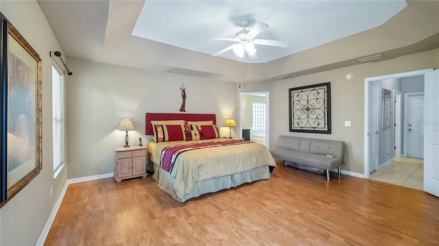 bedroom featuring ceiling fan, a tray ceiling, and light hardwood / wood-style flooring