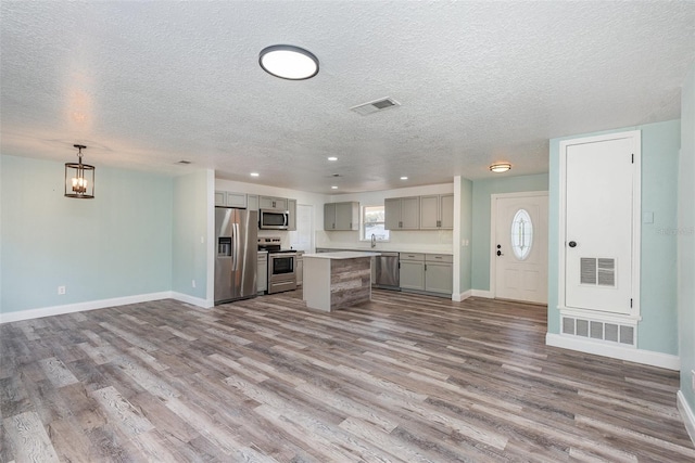 kitchen with pendant lighting, light hardwood / wood-style flooring, appliances with stainless steel finishes, gray cabinetry, and a center island