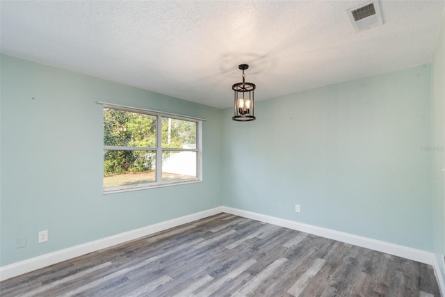 unfurnished room with hardwood / wood-style floors, a notable chandelier, and a textured ceiling