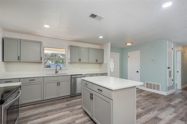 kitchen featuring appliances with stainless steel finishes, gray cabinets, a center island, and sink