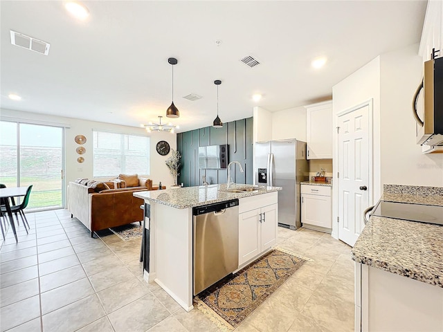 kitchen featuring white cabinets, stainless steel appliances, a kitchen island with sink, and decorative light fixtures