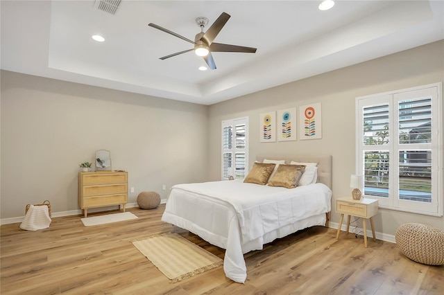 bedroom with ceiling fan, wood-type flooring, and a tray ceiling