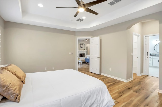 bedroom with ceiling fan, hardwood / wood-style floors, ensuite bathroom, and a tray ceiling