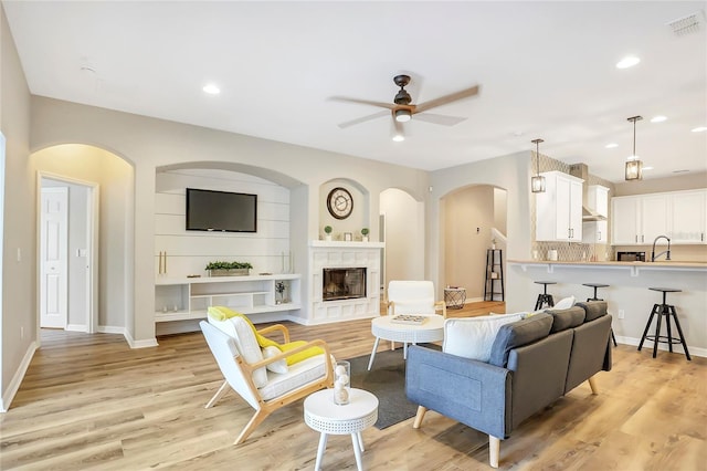 living room with a fireplace, light wood-type flooring, sink, and ceiling fan