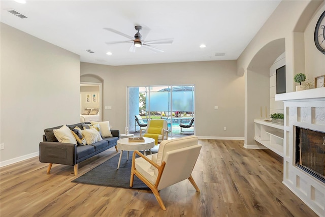 living room with ceiling fan, a high end fireplace, built in shelves, and light hardwood / wood-style floors