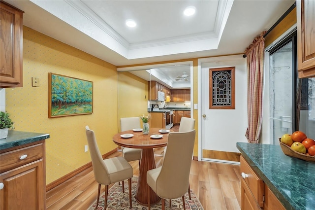 dining area featuring wallpapered walls, a tray ceiling, light wood finished floors, and crown molding