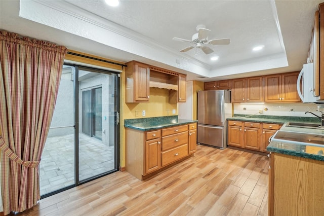 kitchen with dark countertops, a raised ceiling, white microwave, freestanding refrigerator, and a sink