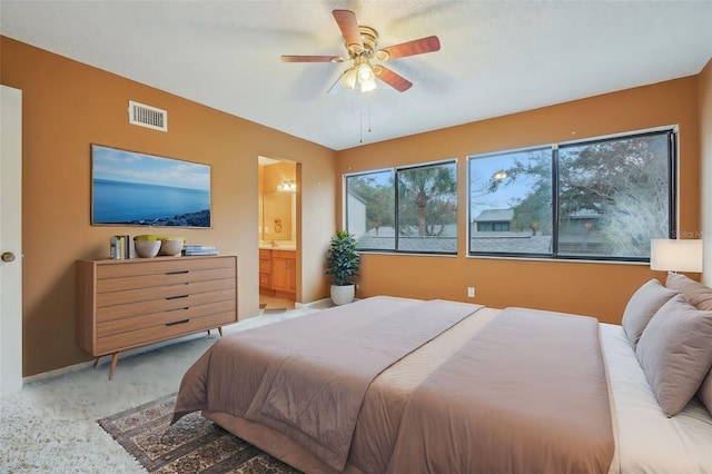 bedroom featuring light carpet, visible vents, baseboards, ensuite bath, and ceiling fan