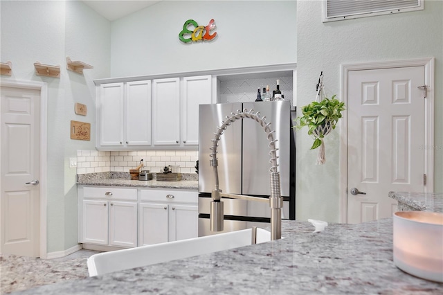 kitchen with tasteful backsplash, stainless steel fridge, light stone countertops, and white cabinets