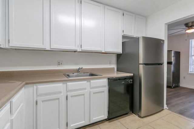 kitchen featuring sink, white cabinets, light tile patterned floors, black dishwasher, and stainless steel refrigerator