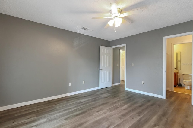 unfurnished bedroom featuring ceiling fan, wood-type flooring, a textured ceiling, and ensuite bath