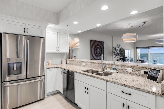 kitchen with a sink, stainless steel appliances, light stone counters, and white cabinetry