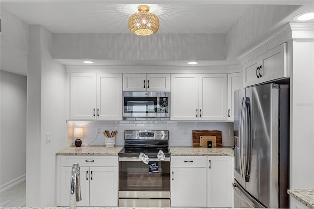 kitchen with light stone countertops, backsplash, appliances with stainless steel finishes, and white cabinets