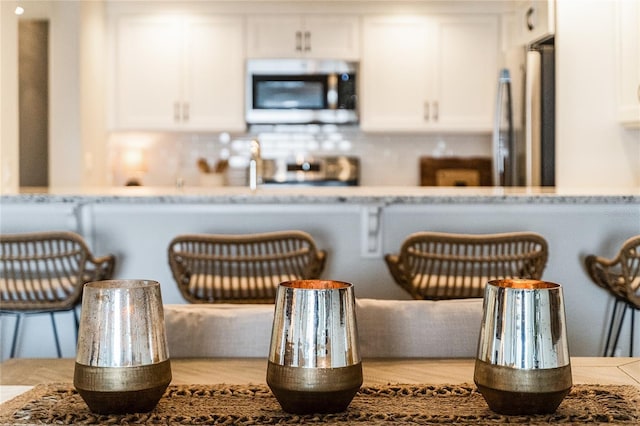 kitchen with light stone counters, stainless steel appliances, backsplash, and white cabinetry