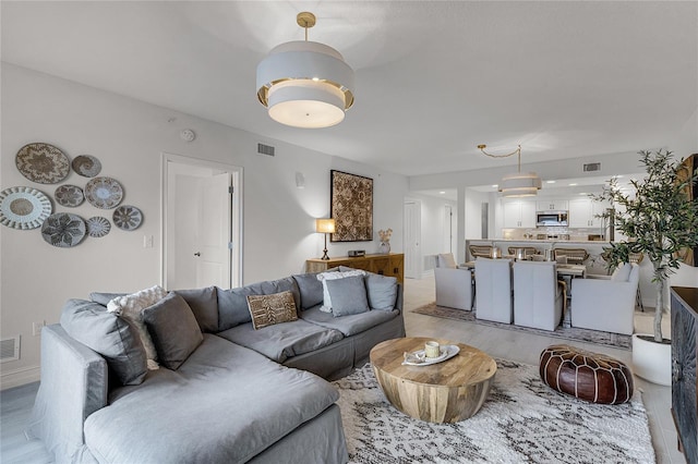 living room with light wood-style floors, visible vents, and baseboards