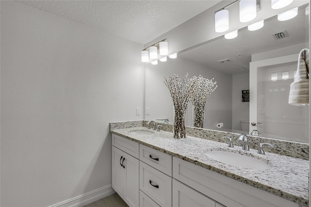 bathroom featuring double vanity, visible vents, a textured ceiling, and a sink