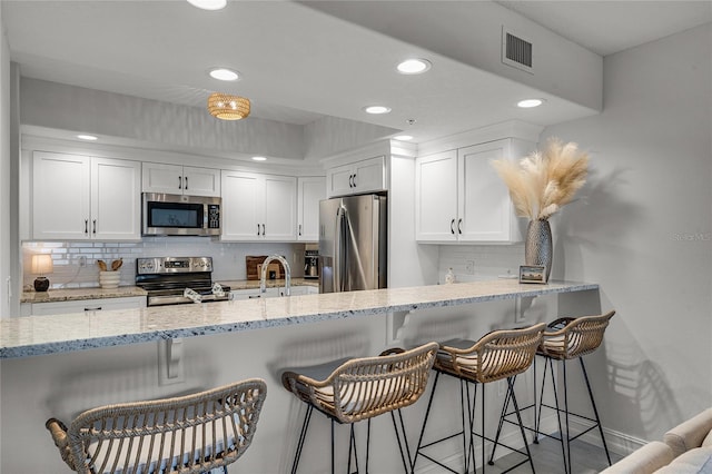 kitchen with visible vents, backsplash, appliances with stainless steel finishes, white cabinets, and light stone countertops