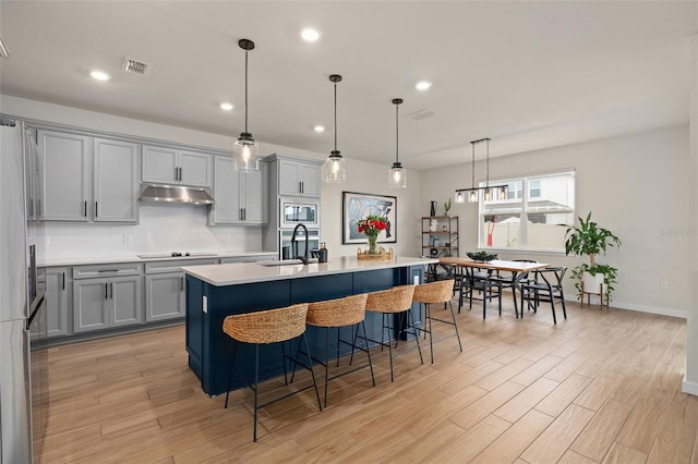 kitchen featuring a breakfast bar, decorative light fixtures, sink, stainless steel appliances, and a center island with sink