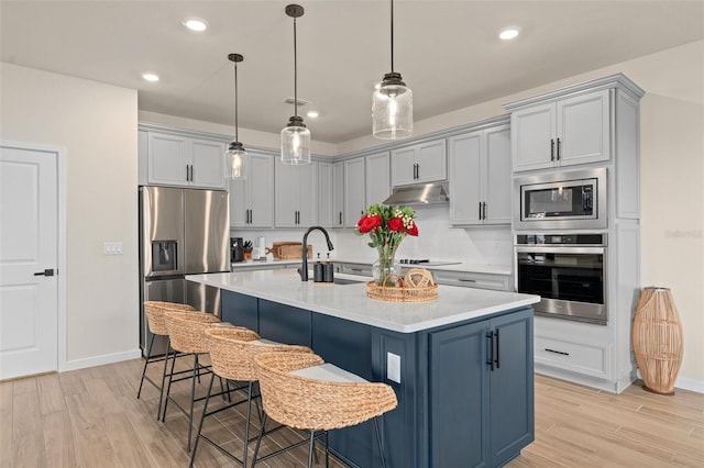 kitchen with a kitchen bar, sink, a center island with sink, light hardwood / wood-style flooring, and appliances with stainless steel finishes