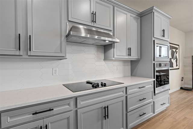 kitchen with gray cabinetry, light stone counters, light hardwood / wood-style flooring, appliances with stainless steel finishes, and decorative backsplash