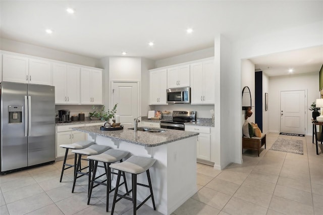 kitchen with light stone counters, white cabinets, a center island with sink, and stainless steel appliances