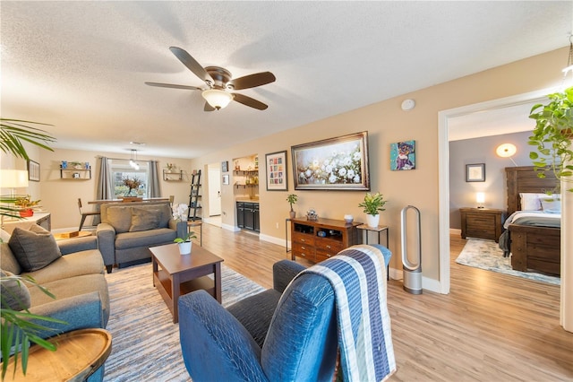 living room featuring ceiling fan, a textured ceiling, and light hardwood / wood-style floors