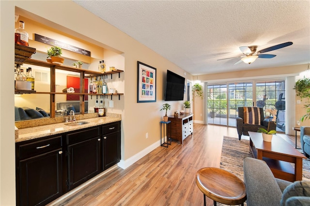 bar with sink, ceiling fan, light stone counters, light hardwood / wood-style floors, and a textured ceiling