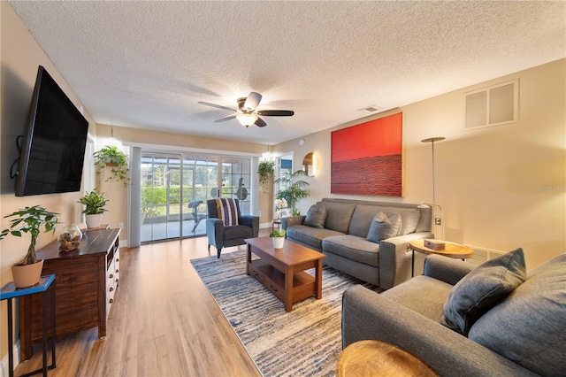 living room with a textured ceiling, light hardwood / wood-style flooring, and ceiling fan