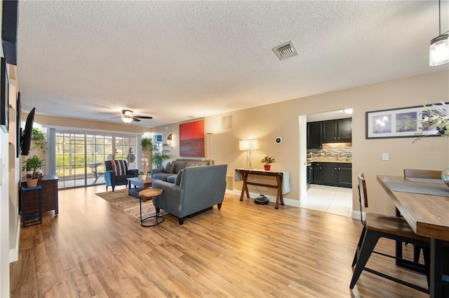 living room with ceiling fan, light hardwood / wood-style flooring, and a textured ceiling