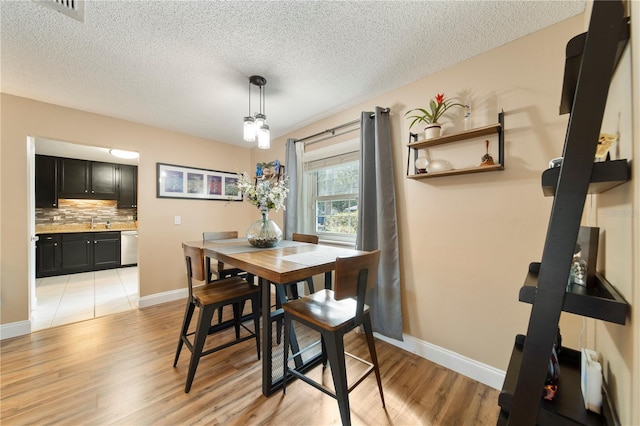 dining room featuring sink, a textured ceiling, and light wood-type flooring