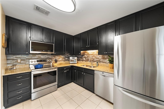 kitchen featuring appliances with stainless steel finishes, sink, decorative backsplash, light tile patterned floors, and light stone countertops