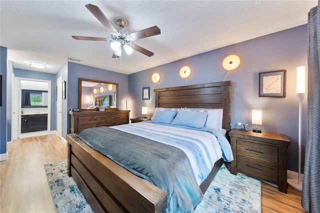 bedroom with ceiling fan, ensuite bath, a textured ceiling, and light wood-type flooring