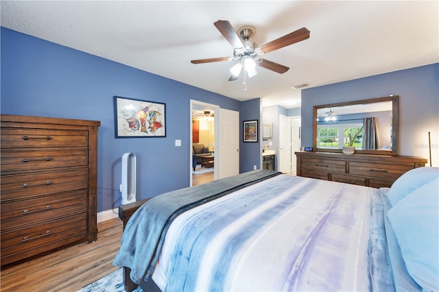 bedroom featuring ceiling fan, light wood-type flooring, a textured ceiling, and ensuite bath