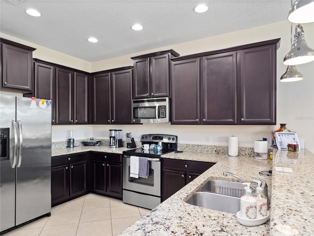 kitchen with hanging light fixtures, sink, stainless steel appliances, light tile patterned flooring, and dark brown cabinetry