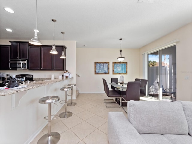 kitchen featuring pendant lighting, a breakfast bar, light tile patterned floors, and light stone counters