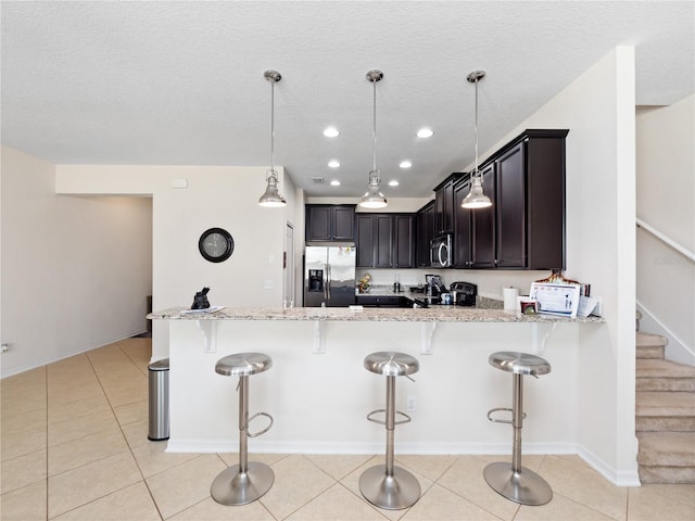 kitchen with pendant lighting, light tile patterned floors, light stone countertops, and appliances with stainless steel finishes